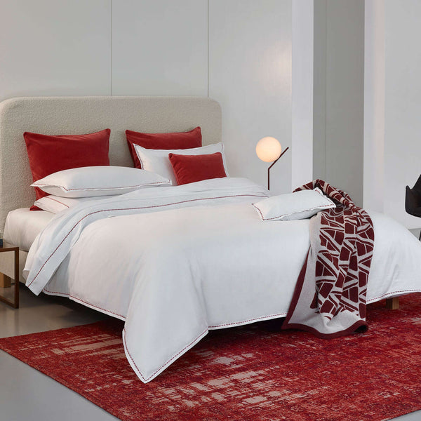 Yves Delorme Nirvana duvet cover in Blanc, styled with crimson velvet pillows and patterned throw.