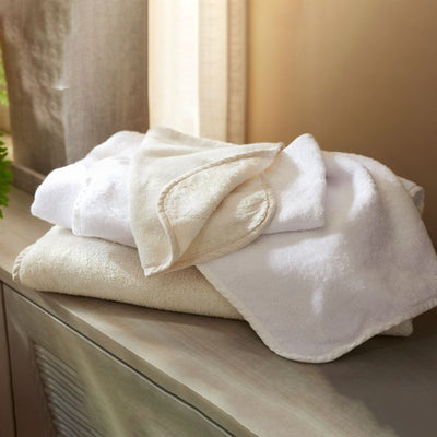 Sferra Legna Terry bath towels in ivory and white stacked on a wooden dresser.