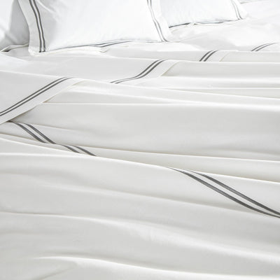 White bed sheets and pillows with gray stripes are neatly arranged on a bed.