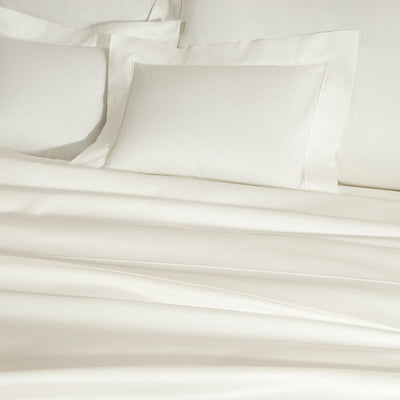 Neatly made bed with smooth, cream-colored sheets and two matching pillowcases, shown in soft lighting.