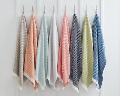 Eight striped towels in various colors hang on individual hooks against a white paneled wall.