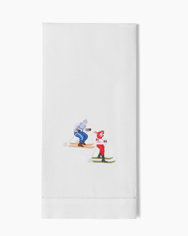 White linen hand towel with hemstitch border and embroidered skiing figures in red and blue.