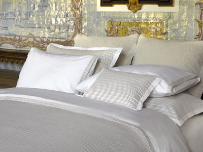 A neatly made bed with white and light gray striped bedding and pillows, set against a decorative wall with ornate patterns.