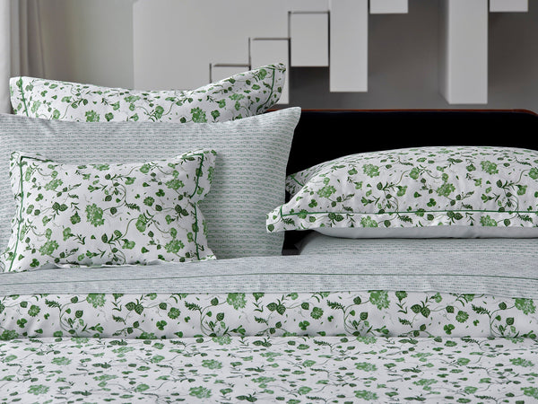 Bed with patterned white and green floral bedding, including pillows and sheets, set against a modern white and gray geometric background.