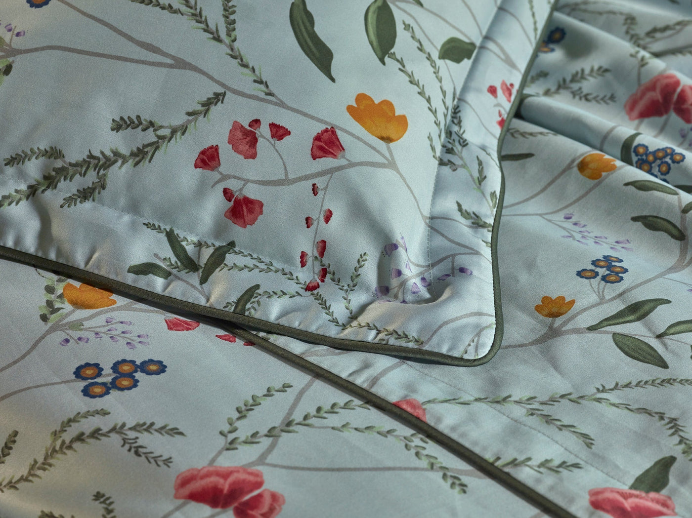 Close-up of light blue bedding with a floral pattern featuring red, yellow, orange, and blue flowers with green leaves.