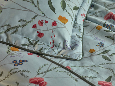 Close-up of light blue bedding with a floral pattern featuring red, yellow, orange, and blue flowers with green leaves.