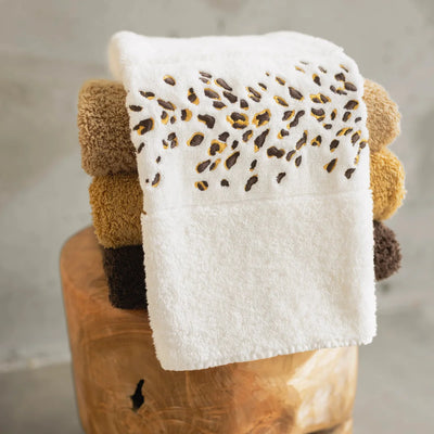 Abyss ivory cotton hand towel with leopard print embroidered border stacked on wood stool.