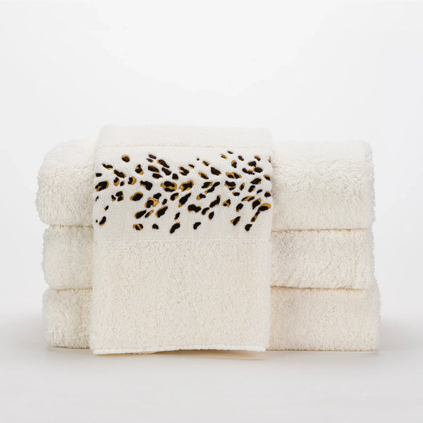 A stack of four white towels, with one towel draped in front featuring a leopard print pattern on the edge.
