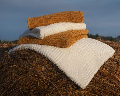Three folded towels—two brown and one white—are stacked on top of a white towel draped over a hay bale outdoors.