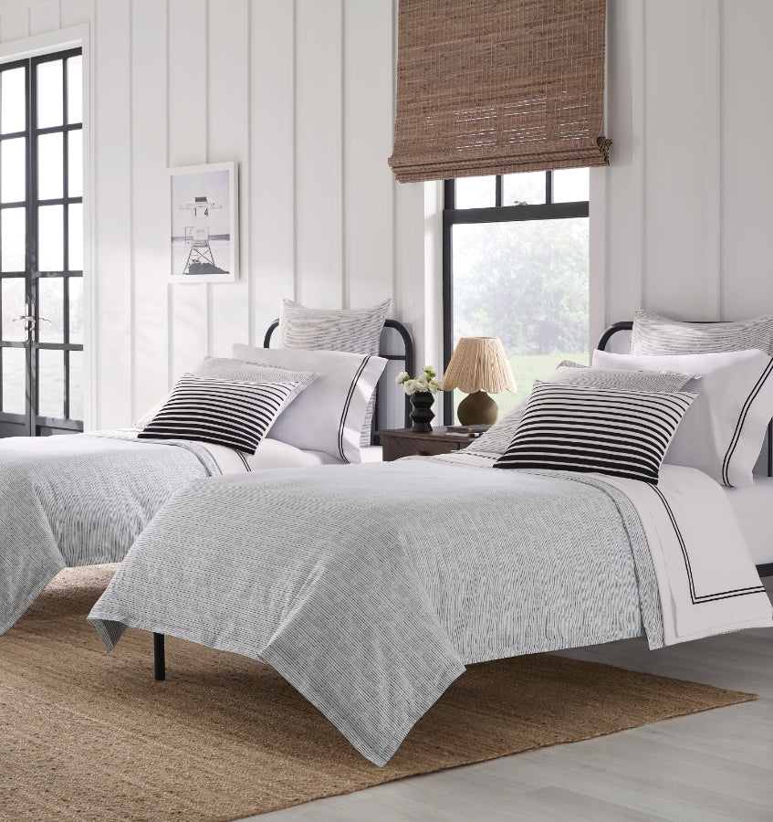 Arzano gray textured duvet covers on twin beds with black stripe accent pillows.