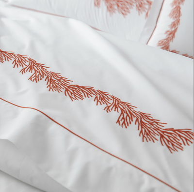 White bedding with orange embroidered coral pattern and matching orange piping, shown in close-up.