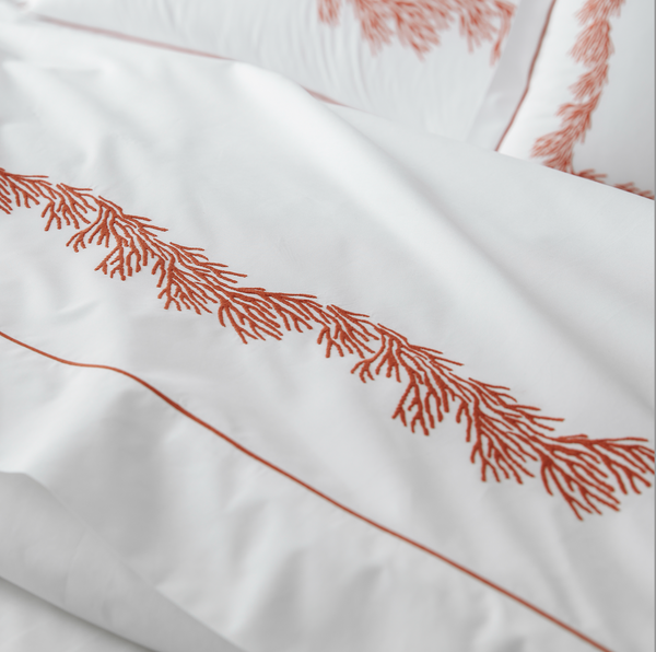 White bedding with orange embroidered coral pattern and matching orange piping, shown in close-up.