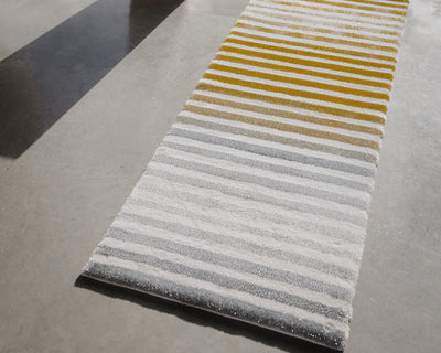 A rectangular rug with yellow and gray horizontal stripes lies on a smooth, light gray floor, partially in sunlight and shadow.