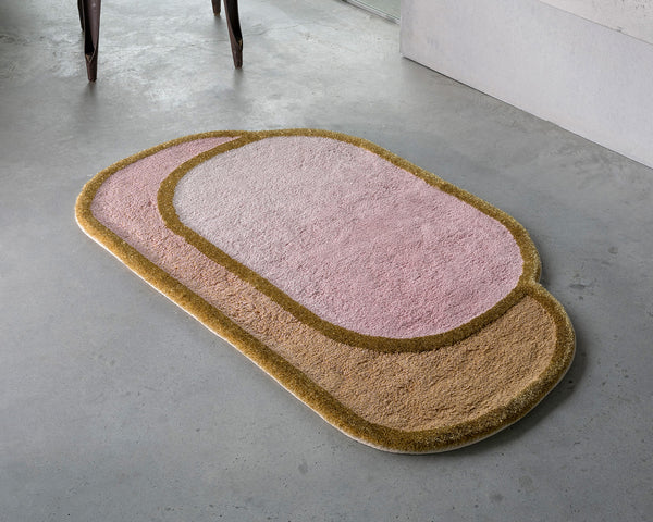 A rug designed to resemble a slice of bread with peanut butter and jelly, placed on a concrete floor near a chair and a wall.