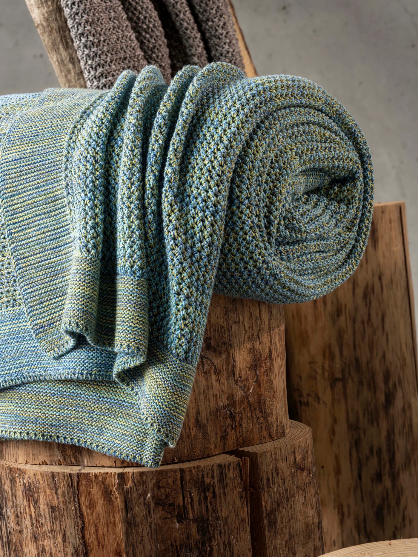 A close-up of a folded gray knit blanket draped over a bed with a geometric patterned white and gray sheet.