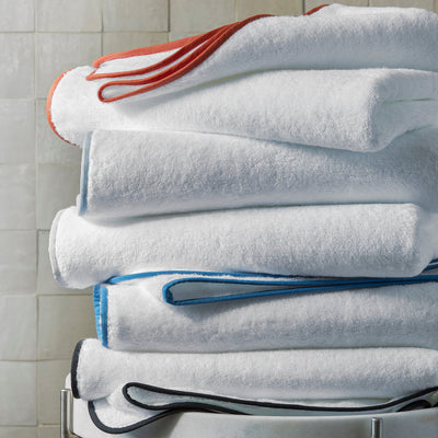 Stack of folded white Egyptian cotton bath towels with colorful contrast border trim on a rack.