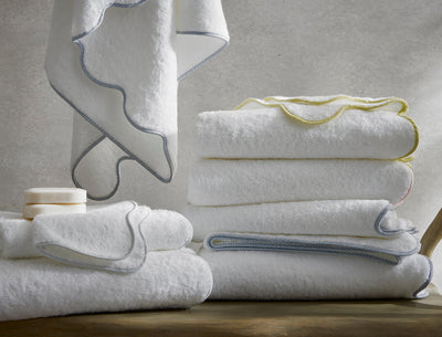 Matouk Jasper white cotton bath towels with scalloped trim in blue, yellow, and gray.