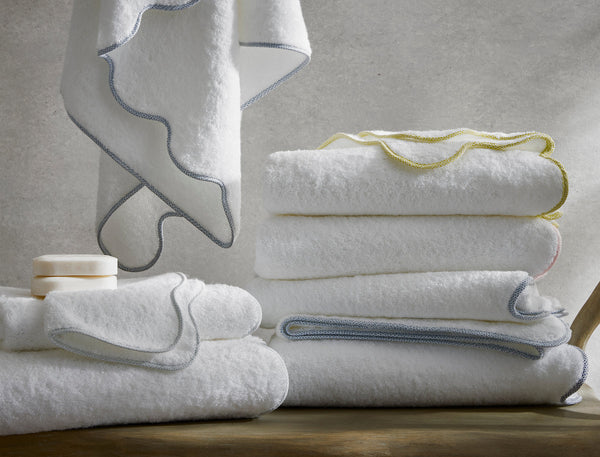Matouk Jasper white cotton bath towels with scalloped trim in blue, yellow, and gray.