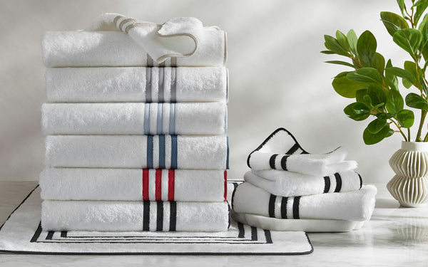 Matouk Newport white cotton bath towels stacked, with striped borders in navy, red, and charcoal.