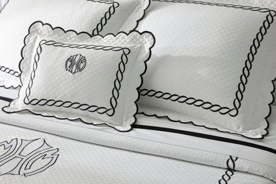 White bedding set with quilted texture, black embroidered borders, and monogram detail on pillows and duvet cover.