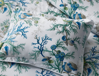 A white pillowcase and sheets with a blue and green sea life print featuring coral, shells, and marine plants.