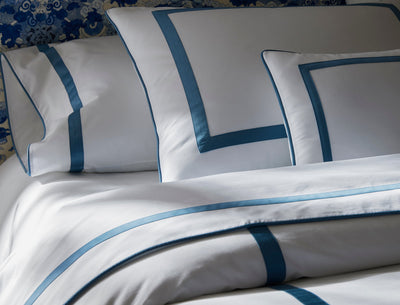 White bedding with blue borders, including pillows and a duvet, neatly arranged on a bed.