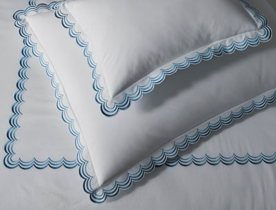 White pillowcases and sheet with scalloped blue embroidery along the borders, neatly arranged on a bed.