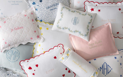 Assorted decorative pillows with personalized embroidery, including names, initials, dates, and phrases, arranged on a white surface.