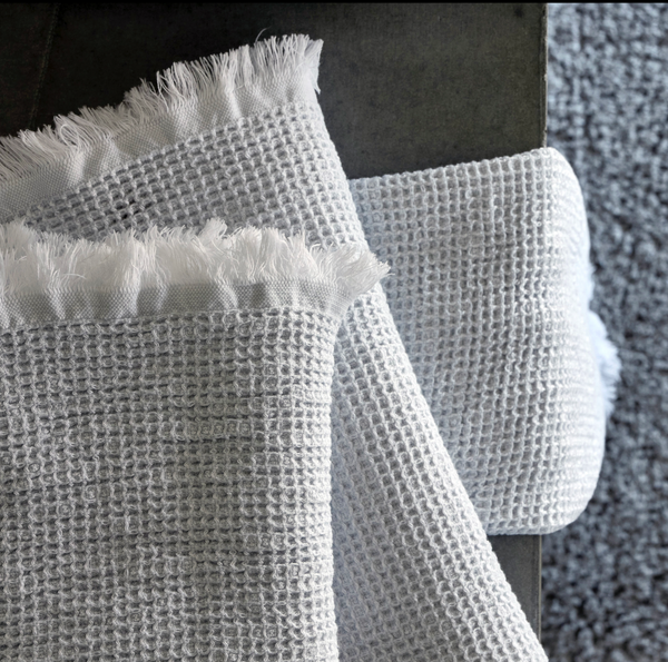 A white waffle-textured towel with fringed edges is draped over the edge of a dark surface, with a grey textured carpet visible in the background.