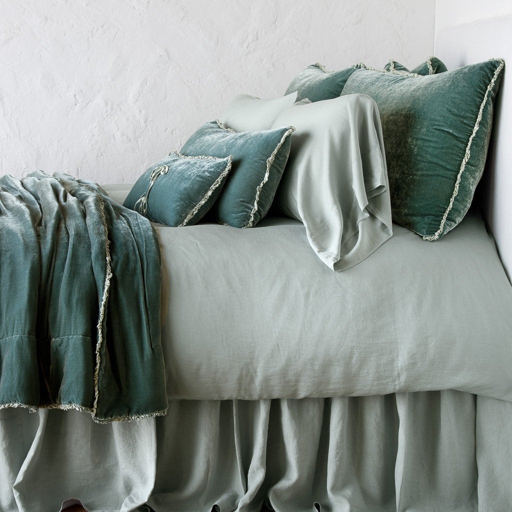 Eucalyptus velvet throw pillows with fringe trim styled on a sage linen bed.