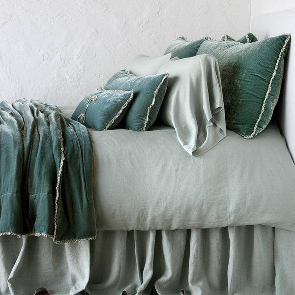 Eucalyptus velvet throw pillows with fringe trim styled on a sage linen bed.