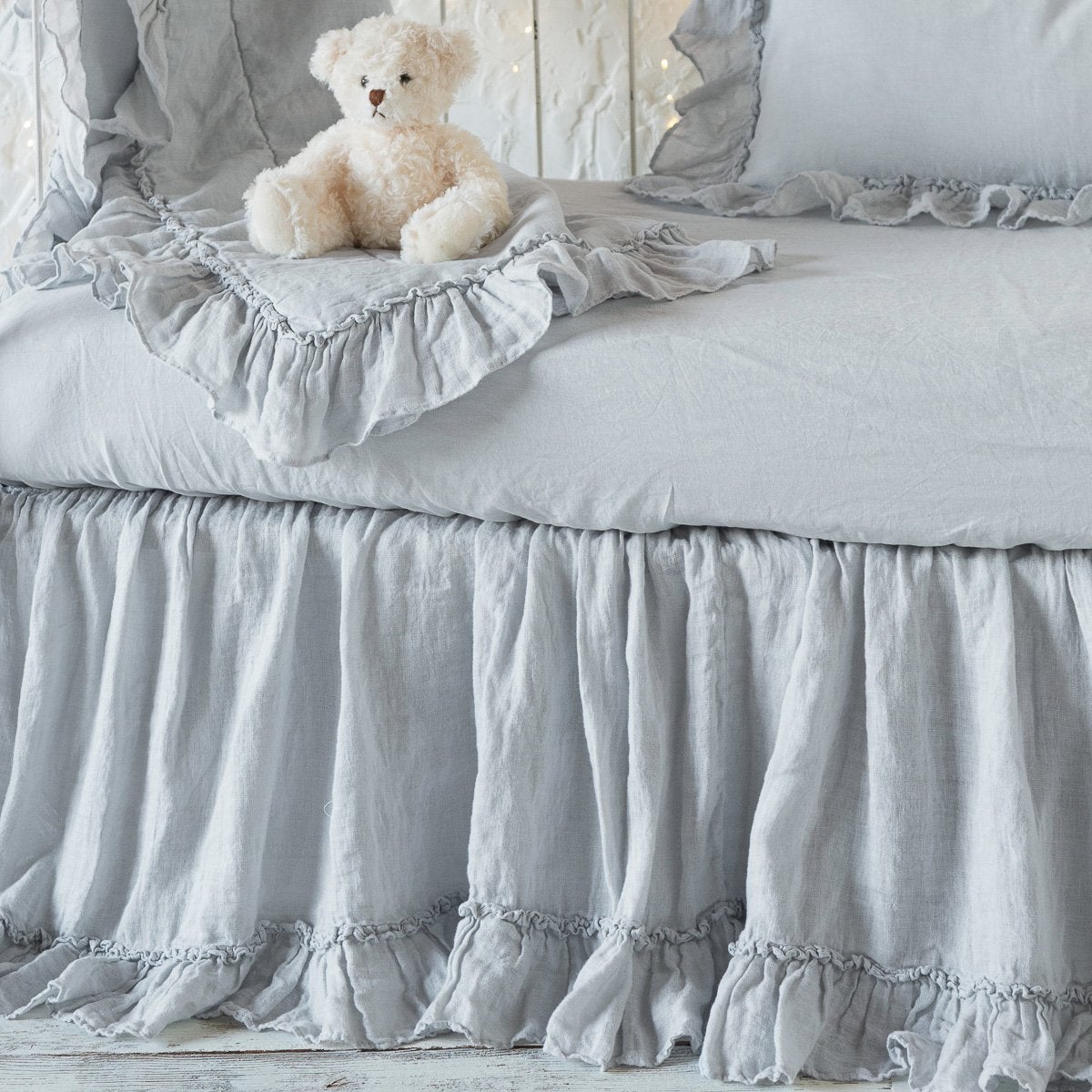 Bella Notte Linen Whisper crib skirt in Cloud with ruffle trim, styled with matching bedding and teddy bear.