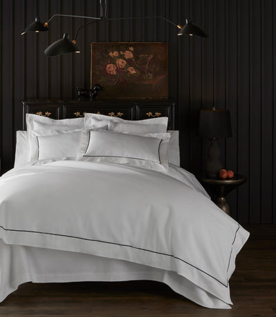 Soprano II white bedding with black satin-stitch border, styled on bed in dark dramatic bedroom.