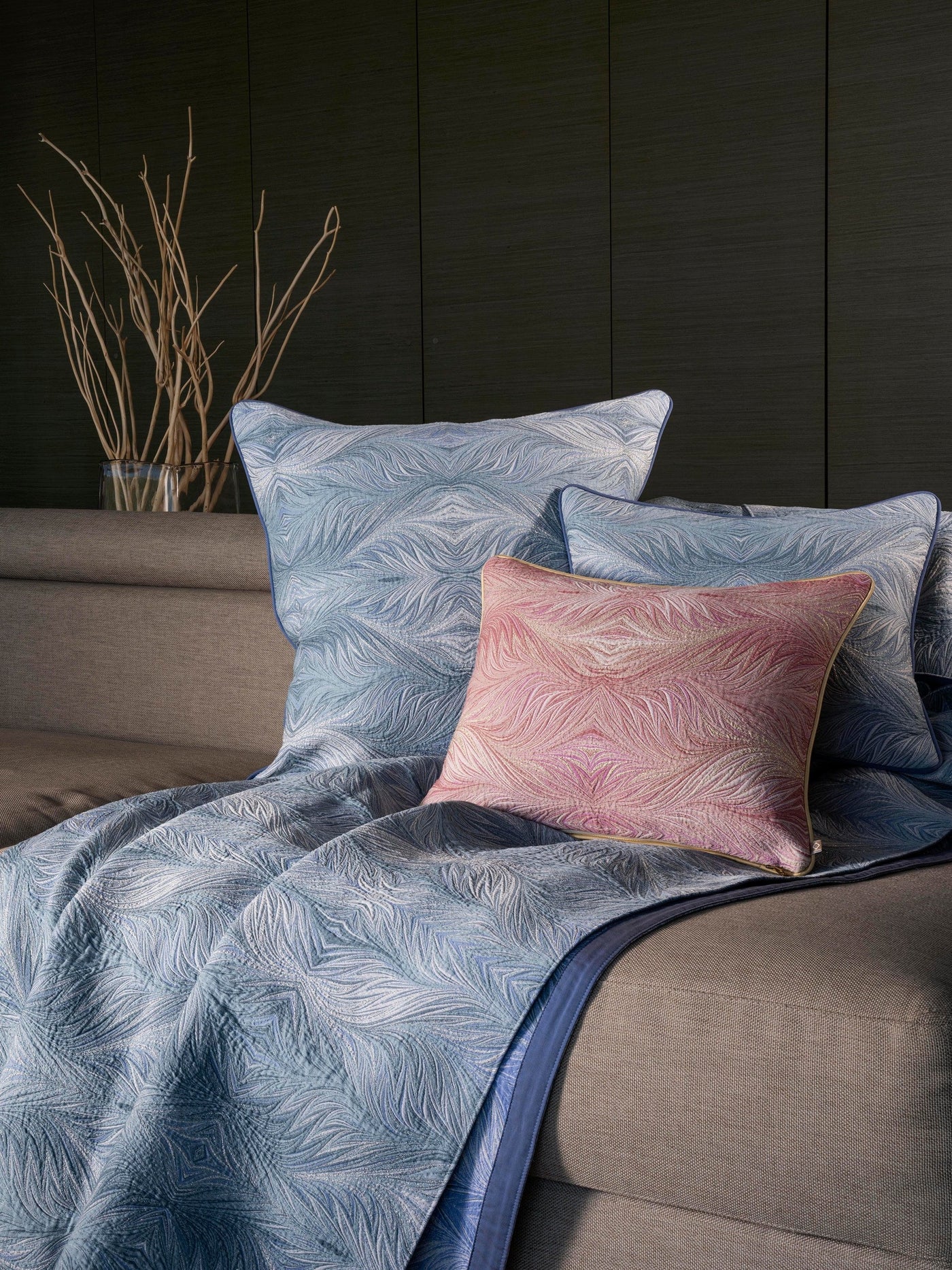 Boheme blue quilted coverlet with feather pattern and blush accent pillow on bed.