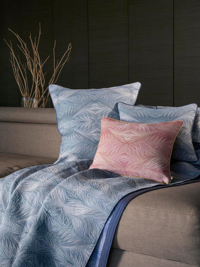 Boheme blue quilted coverlet with feather pattern and blush accent pillow on bed.