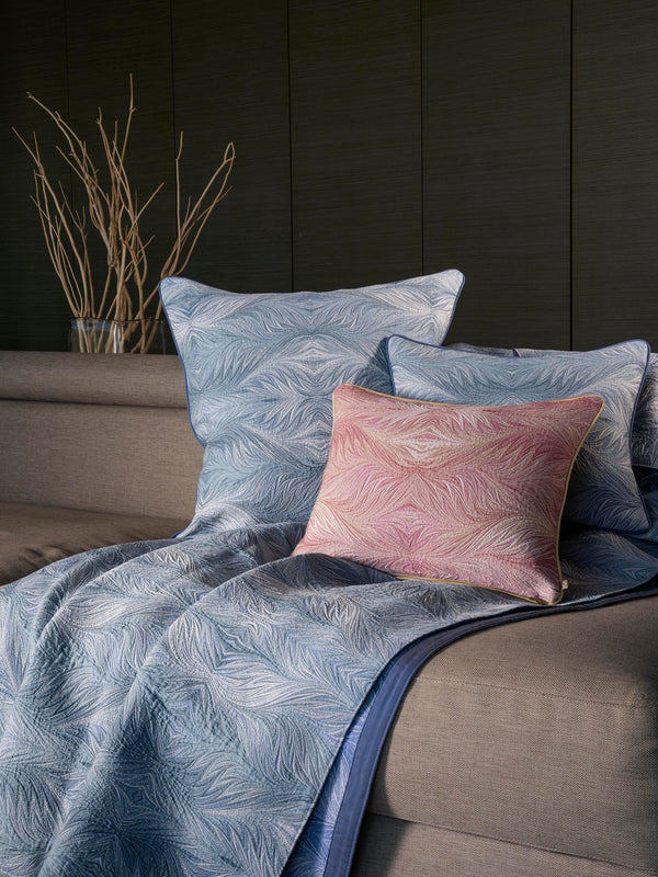 Boheme blue quilted coverlet with feather pattern and blush accent pillow on bed.