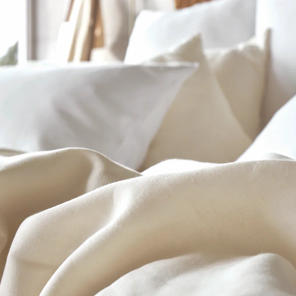 A close-up view of a bed with cream-colored sheets and several white and beige pillows arranged against the headboard.