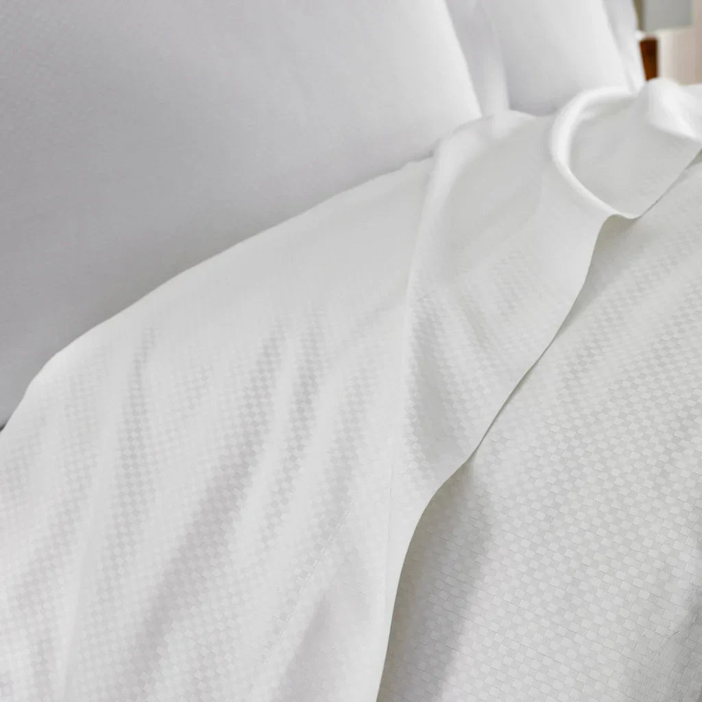 Close-up of a neatly made bed with white textured sheets and pillowcases.