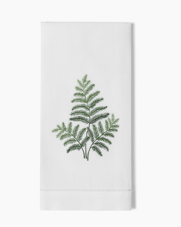White linen hand towel with green embroidered fern motif and hemstitch border.