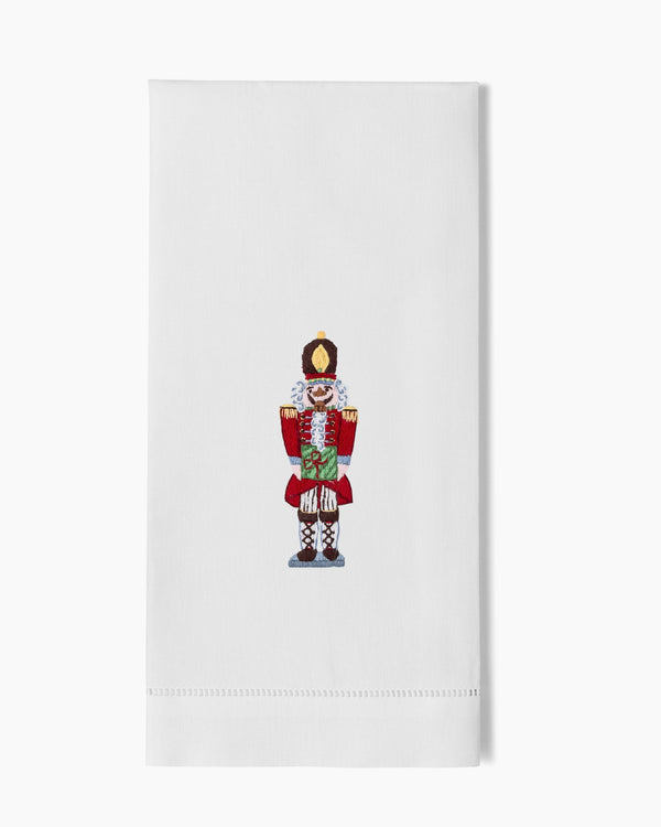 White linen hand towel with embroidered nutcracker soldier in red and gold.