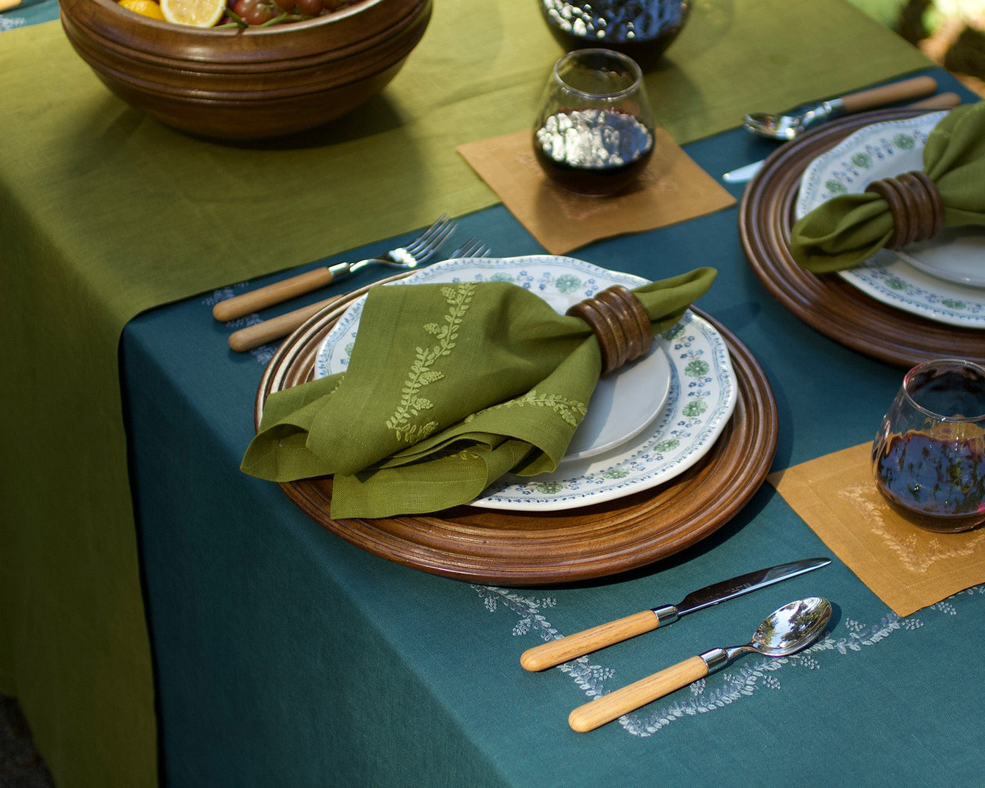 Henry Handwork teal linen tablecloth with olive napkin and embroidered dinnerware place setting.