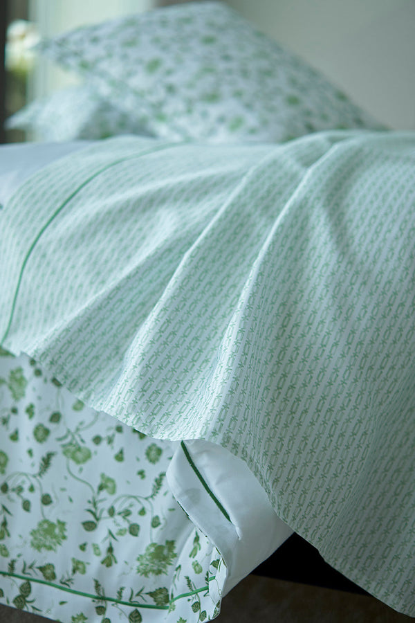 A close-up of a neatly made bed with light green patterned sheets, matching pillowcases, and a floral-patterned bed skirt.
