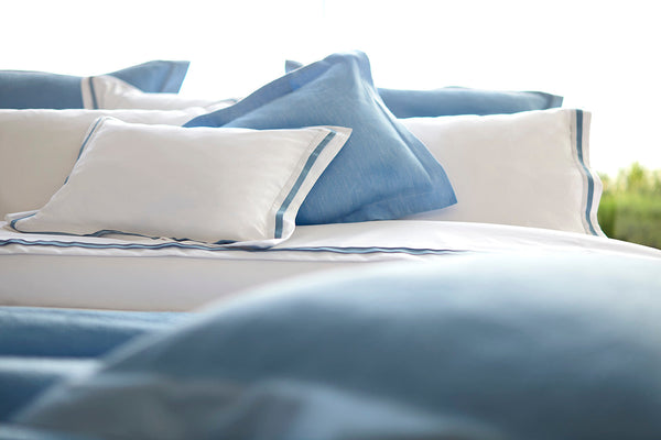 A neatly made bed with white and light blue pillows and linens, arranged in layers, with a soft and inviting appearance.