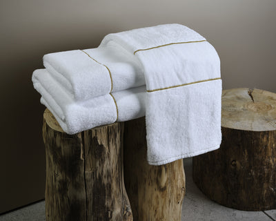 Three neatly folded white towels with gold trim are stacked on two wooden tree stumps, with one towel draped over the top.