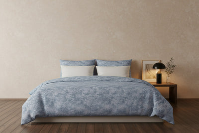 A bed with a blue blanket and a black lamp on a nightstand.