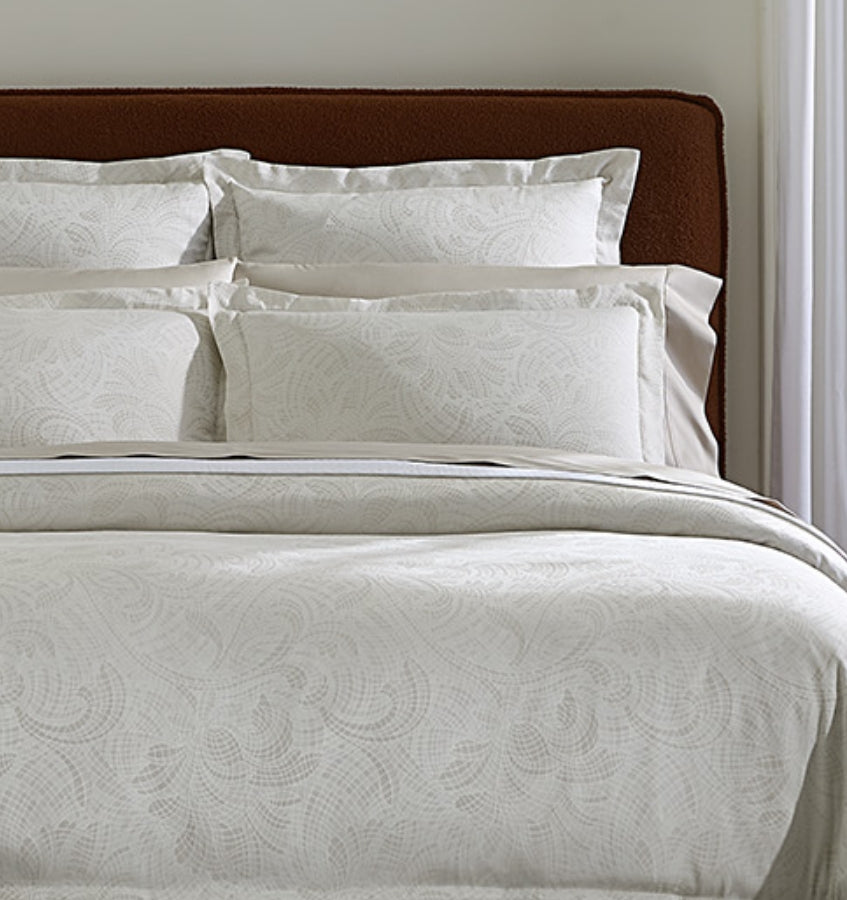 Sferra Leonessa ivory jacquard bedding set with swirl pattern on made bed.