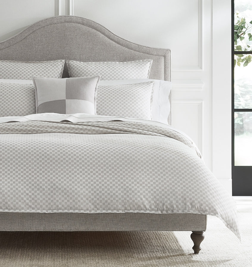 Sferra Macchia silver and white checkered cotton bedding set on upholstered bed.