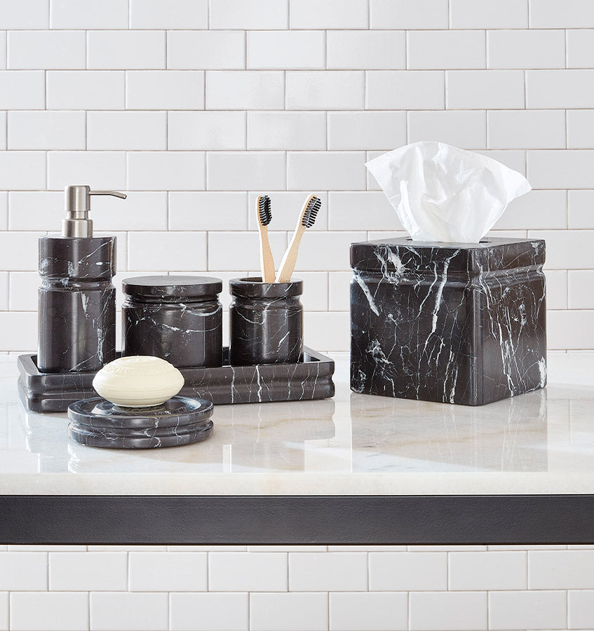 Marquina black marble bathroom accessory set on white countertop with subway tile.