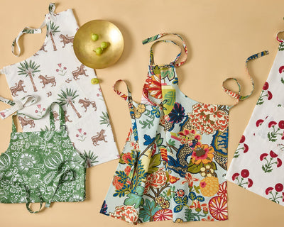 Matouk printed cotton aprons in floral and tropical patterns on peach background.