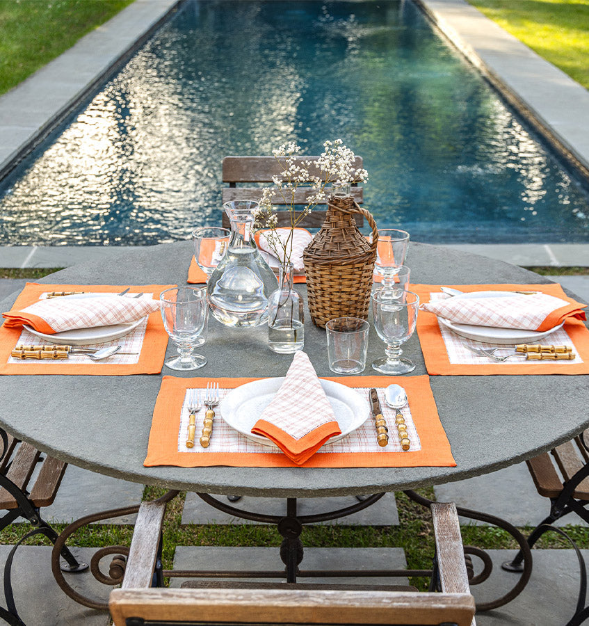 Orange and white check linen napkins and placemats set on outdoor stone table by pool.